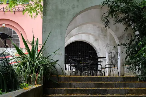 Esplanada com mesas e cadeiras sob arcada, junto a escadas e vegetação no Jardim Botânico Tropical