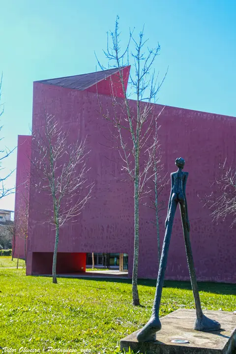Edifício cor-de-rosa da Casa das Artes, com árvores sem folhas e escultura de bronze no relvado