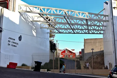 Entrada do Jardim do Caracol da Penha, com letreiro na parede branca e estrutura metálica sobre a rua