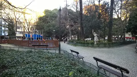 Jardim da Parada com bancos, parque infantil vedado e estátua entre árvores ao fim da tarde