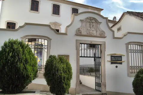 Fachada branca do Museu Municipal Carlos Reis, em Torres Novas, com portão de ferro e letreiro