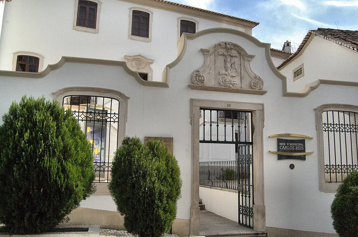 Fachada branca do Museu Municipal Carlos Reis, em Torres Novas, com portão de ferro e letreiro