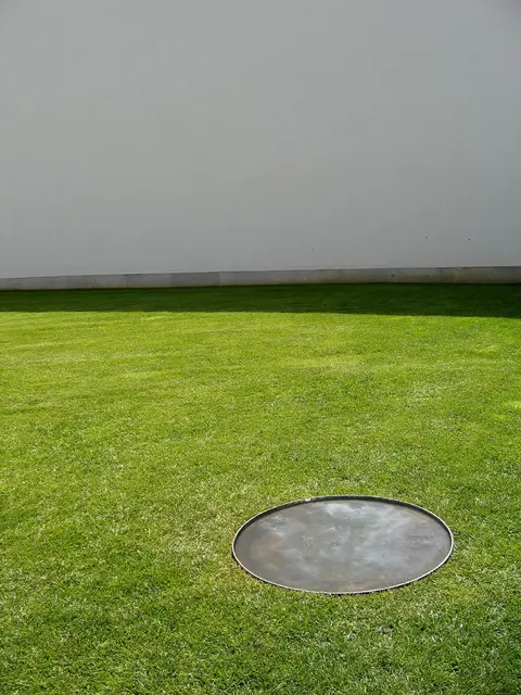 Relvado junto a parede branca do Museu de Serralves com disco metálico circular no chão
