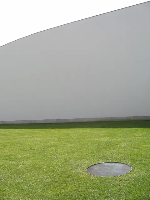 Fachada branca curva do Museu de Serralves sobre relvado com elemento circular metálico
