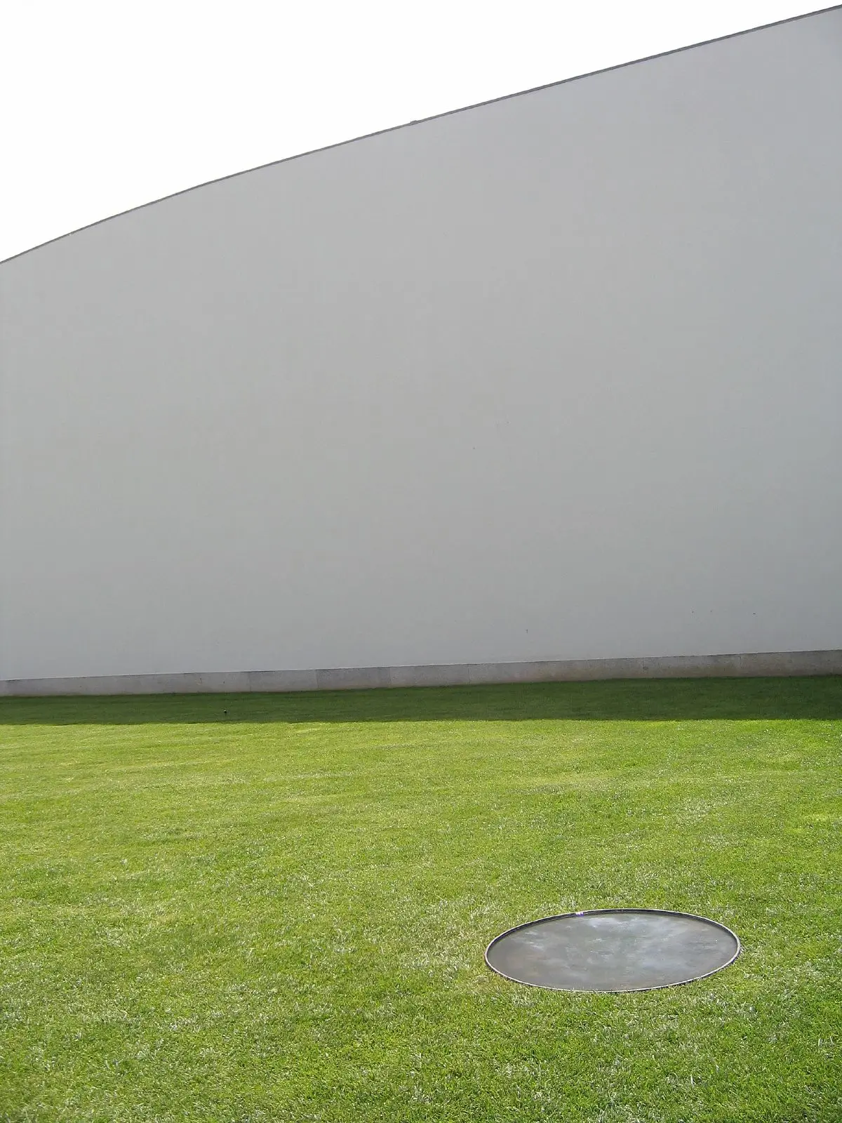 Fachada branca curva do Museu de Serralves sobre relvado com elemento circular metálico