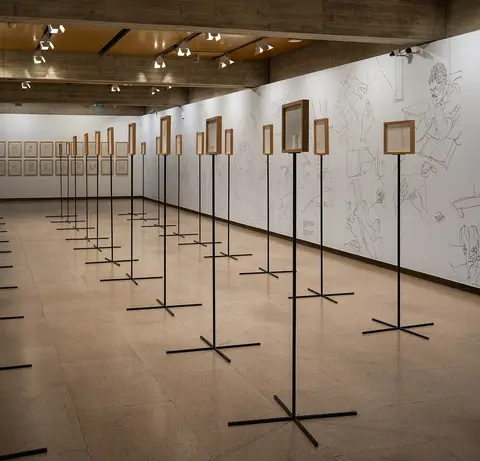 Sala de exposição com molduras em suportes altos e desenhos a traço na parede branca