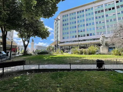 Jardim Camilo Castelo Branco com relvado, árvores, gradeamento e estátua junto a edifício em Lisboa