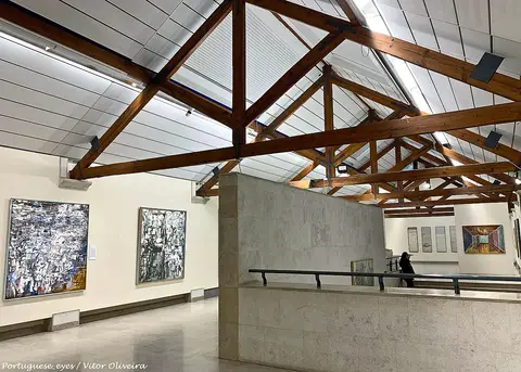 Sala de exposição do Museu Arpad Szenes - Vieira da Silva, com telhado de vigas de madeira e quadros nas paredes