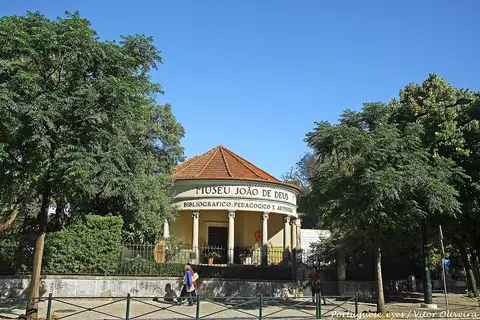 Edifício circular amarelo do Museu João de Deus, em Lisboa, rodeado de árvores.