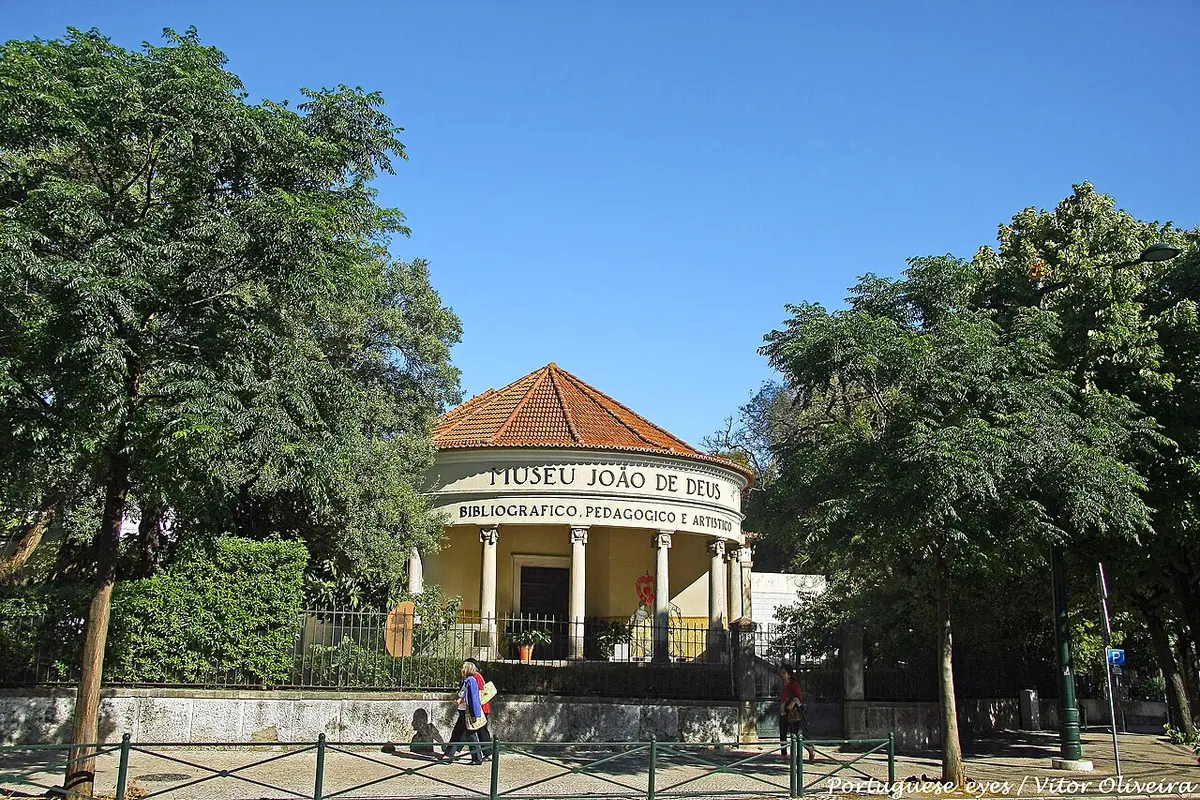 Edifício circular amarelo do Museu João de Deus, em Lisboa, rodeado de árvores.