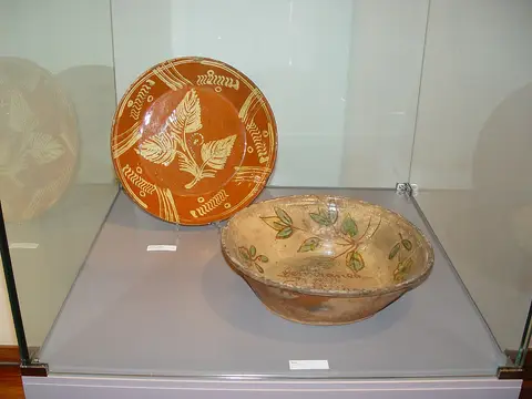 Vitrina de museu com prato e taça de barro vidrado com decoração floral