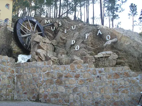 Entrada exterior do Museu do Pão em Seia, com roda de moinho e letras na rocha sobre muro de pedra.