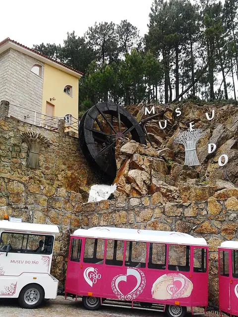 Entrada do Museu do Pão em Seia, com roda de água em pedra e comboio turístico cor-de-rosa