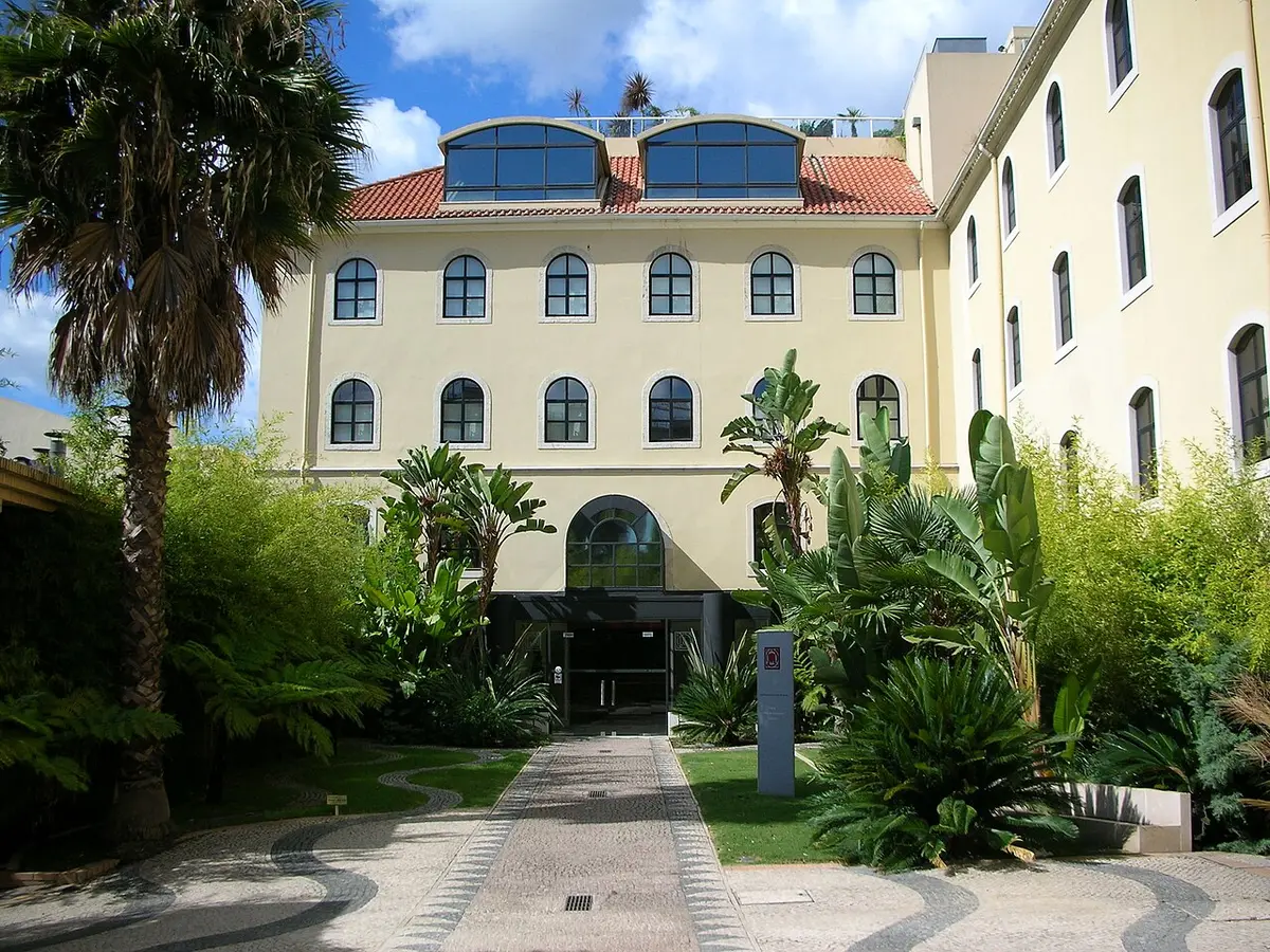 Edifício amarelo do Centro Científico e Cultural de Macau, em Lisboa, com jardim de palmeiras e calçada portuguesa.
