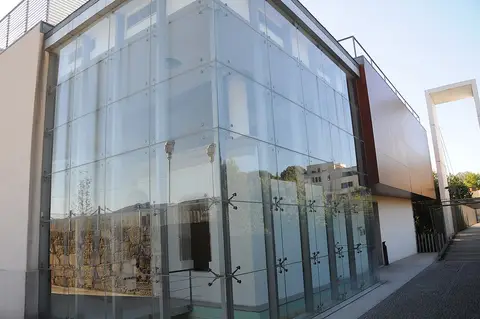 Fachada envidraçada de edifício moderno de museu, com vestígios de muralha visíveis no interior