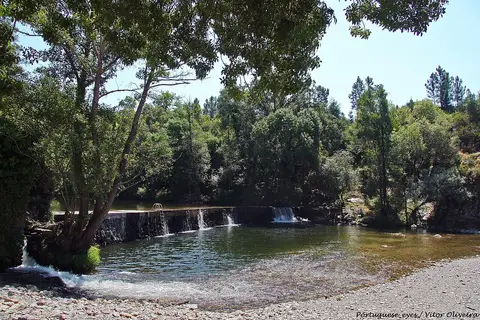 Praia fluvial dos Moinhos de Alva com açude, água corrente e vegetação nas margens