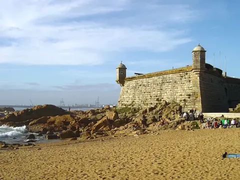 Castelo do Queijo sobre rochas junto à praia de areia, com céu azul e mar ao fundo