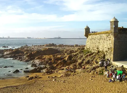 Castelo do Queijo sobre rochas junto à praia, com o mar e o céu azul ao fundo, no Porto