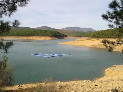 Albufeira de Santa Luzia com pontão flutuante, margens de areia e colinas arborizadas ao fundo