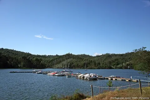 Pontões flutuantes com pequenas embarcações numa albufeira rodeada de encostas arborizadas