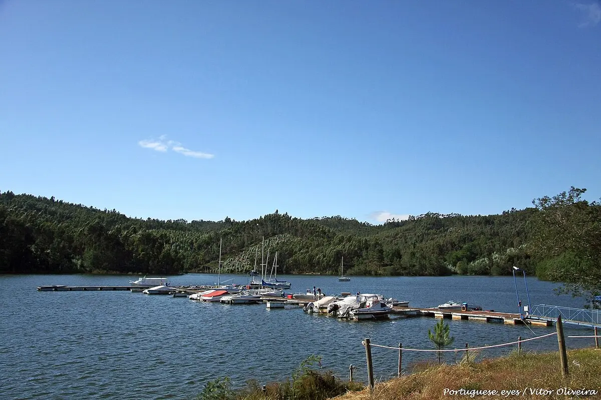 Pontões flutuantes com pequenas embarcações numa albufeira rodeada de encostas arborizadas