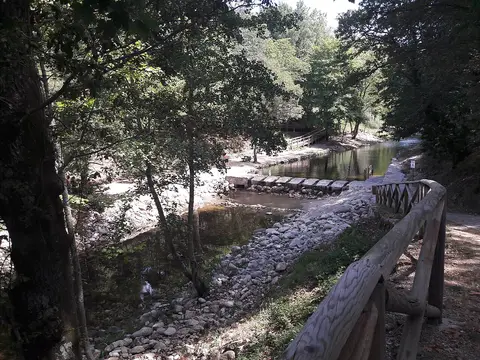Praia fluvial Dr. Pedro em São Romão, Seia, com rio, açude de pedra e corrimão de madeira entre árvores
