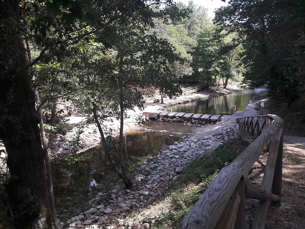 Praia fluvial Dr. Pedro em São Romão, Seia, com rio, açude de pedra e corrimão de madeira entre árvores