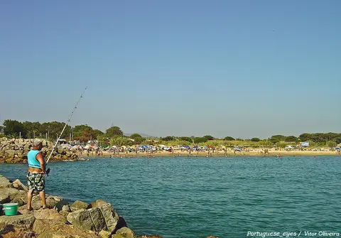 Praia do Forte Novo vista do molhe de rochas, com banhistas ao longe e mar calmo
