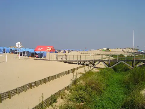 Praia de Miramar com passadiço de madeira, dunas e tendas de praia azuis ao fundo