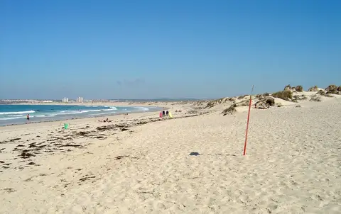 Praia da Cova da Alfarroba com extenso areal, dunas e mar calmo sob céu azul