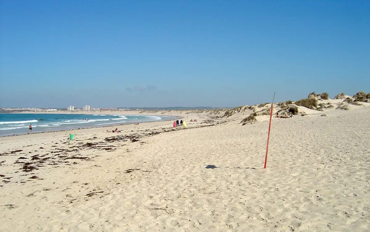 Praia da Cova da Alfarroba com extenso areal, dunas e mar calmo sob céu azul