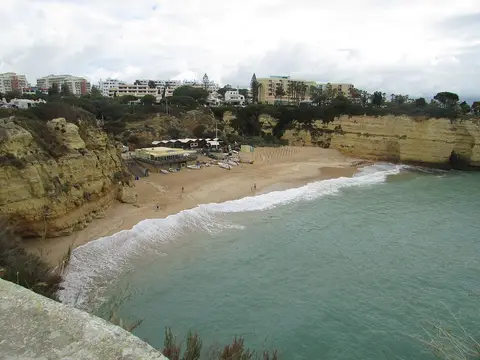 Vista do alto da Praia da Senhora da Rocha, com areal entre falésias e mar esverdeado