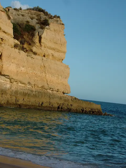 Falésia dourada junto ao mar na praia da Senhora da Rocha, com ondas suaves na areia