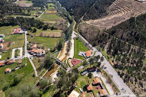 Vista aérea do parque fluvial do Açude do Pinto, com rio, passadiços e casas junto à encosta
