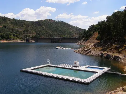 Piscina flutuante na albufeira do Cabril, com a barragem e encostas arborizadas ao fundo
