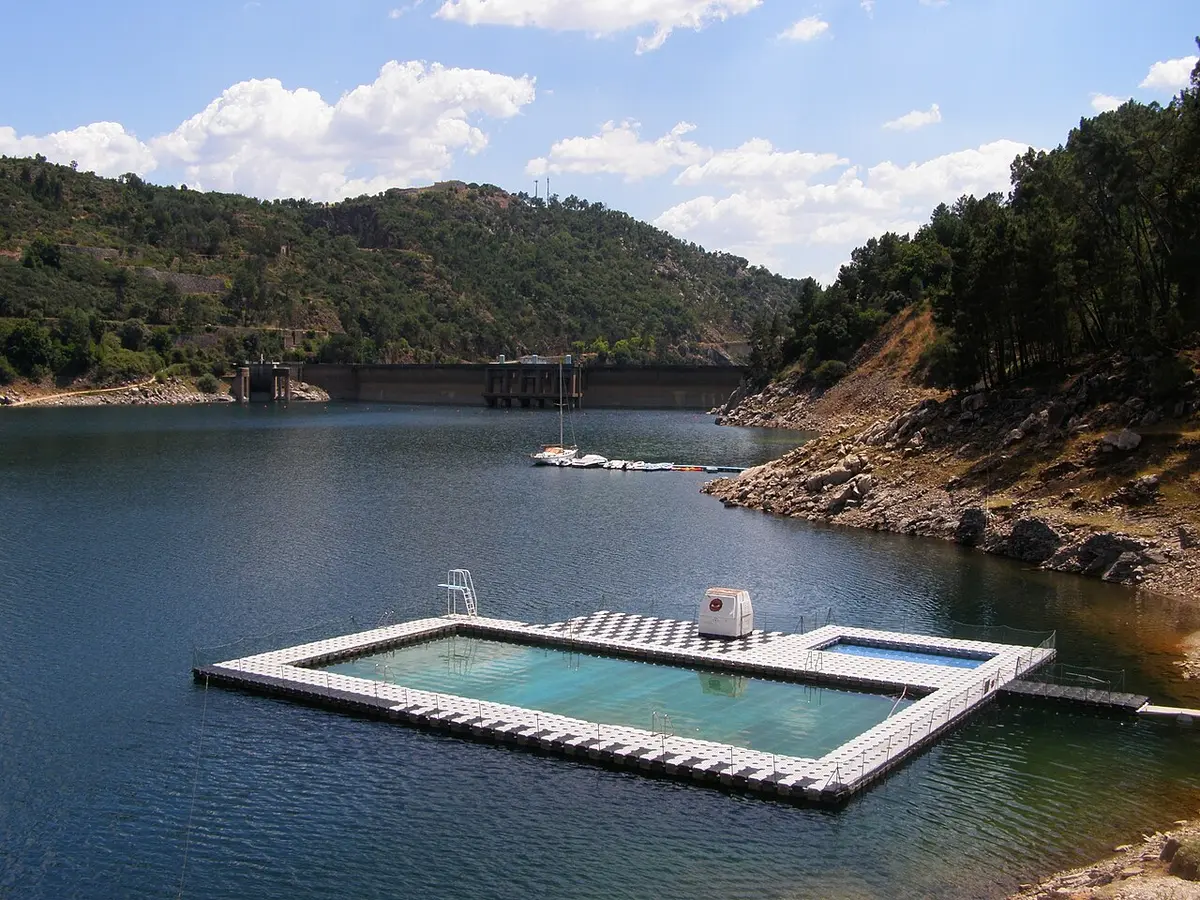 Piscina flutuante na albufeira do Cabril, com a barragem e encostas arborizadas ao fundo