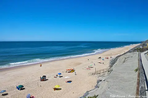 Vista panorâmica da Praia da Pedra do Ouro, com areal extenso, chapéus-de-sol e mar azul.