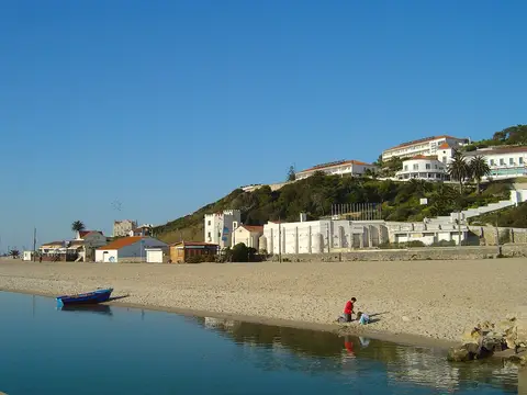 Praia da Foz do Arelho junto à lagoa, com barco na areia e edifícios na encosta