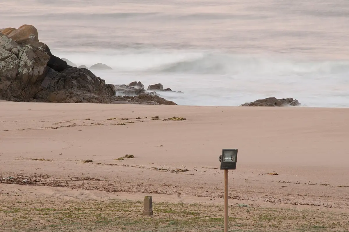 Praia de areia com rochas e mar ao entardecer, junto a Santo André