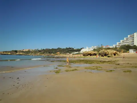 Praia da Oura em Albufeira com areal extenso, falésias e edifícios ao fundo sob céu azul