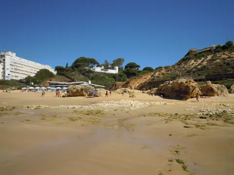 Praia da Oura em Albufeira, com areal amplo, rochas douradas e edifícios sobre a arriba