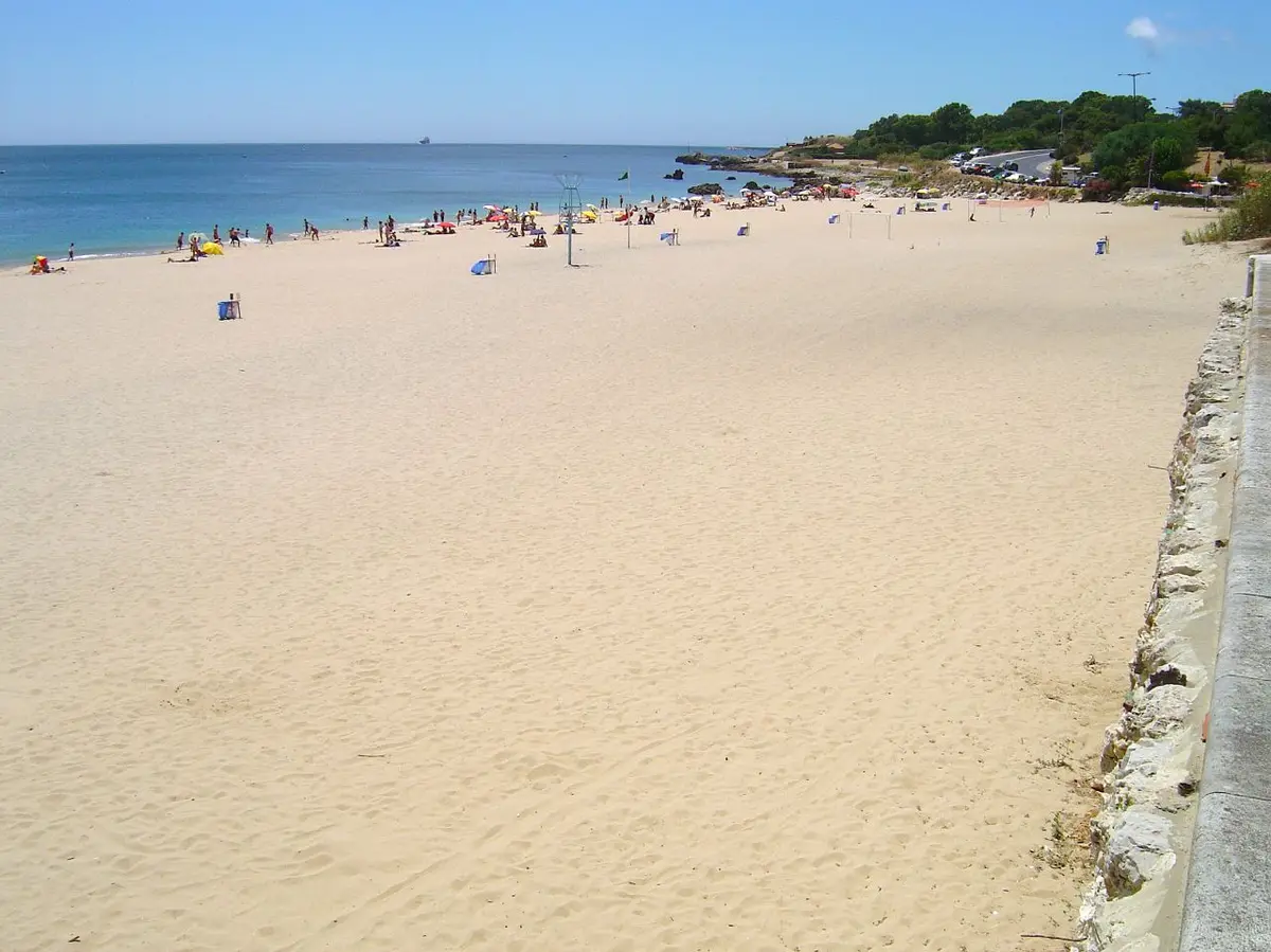 Areal extenso da praia de Paço de Arcos com banhistas ao longe junto ao mar, em dia de céu limpo