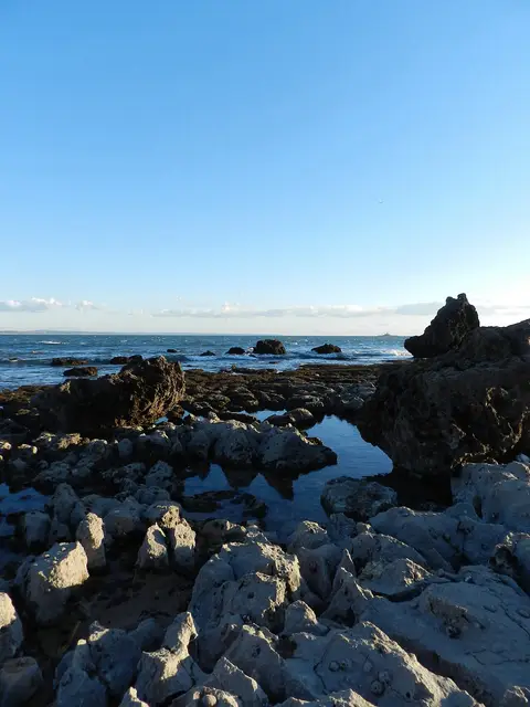 Formações rochosas e poças de maré junto à praia de Paço de Arcos, com o mar e céu azul ao fundo