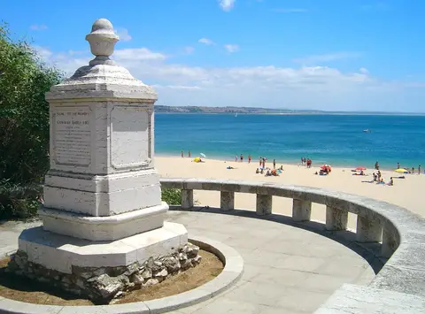 Monumento "Túmulo do Inglês" em miradouro sobre a praia de Paço de Arcos, com mar azul ao fundo