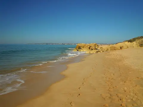 Praia da Galé com areia dourada, falésias baixas e mar calmo sob céu azul