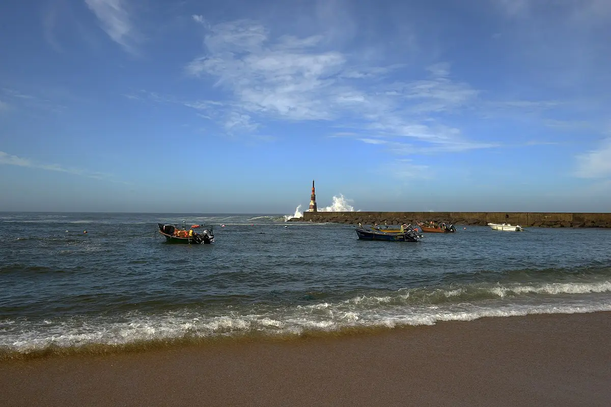 Praia da Aguda com barcos de pesca ancorados junto ao quebra-mar e farol ao fundo