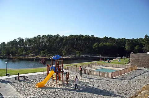 Praia fluvial do Trabulo com parque infantil, areia e piscina junto ao rio rodeada de pinhal