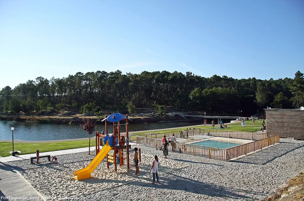 Praia fluvial do Trabulo com parque infantil, areia e piscina junto ao rio rodeada de pinhal