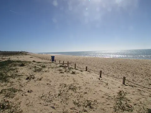 Praia dos Salgados com areal extenso, dunas com vegetação rasteira e mar calmo ao sol