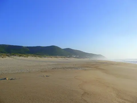 Praia de areia extensa em Quiaios, com serra verde ao fundo e céu limpo